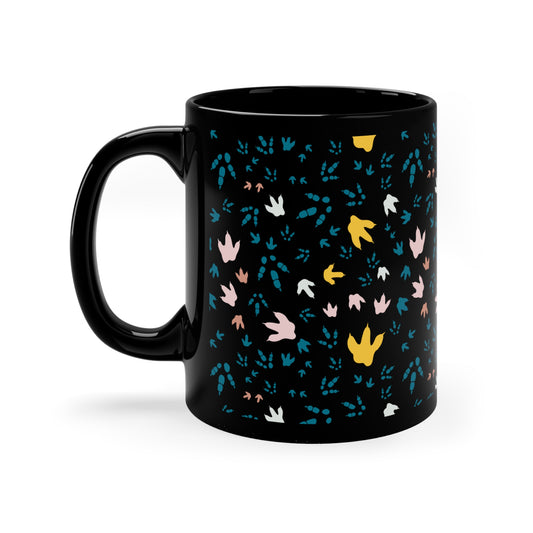 Front view of black mug with multicolored dinosaur footprint pattern